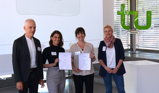 Vier Personen stehen nebeneinander und halten Urkunden hoch.