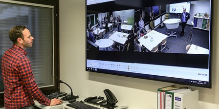 Person steht vor großem Bildschirm mit Kameras