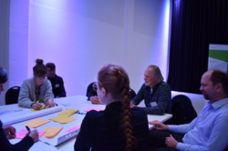 einige Personen sitzen an einem Tisch zusammen, diskutieren und schreiben Ergebnisse auf Zettel