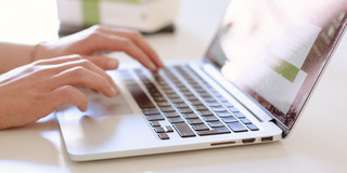 Arbeit am Laptop Studentin tippend am Laptop, daneben liegen Bücher.